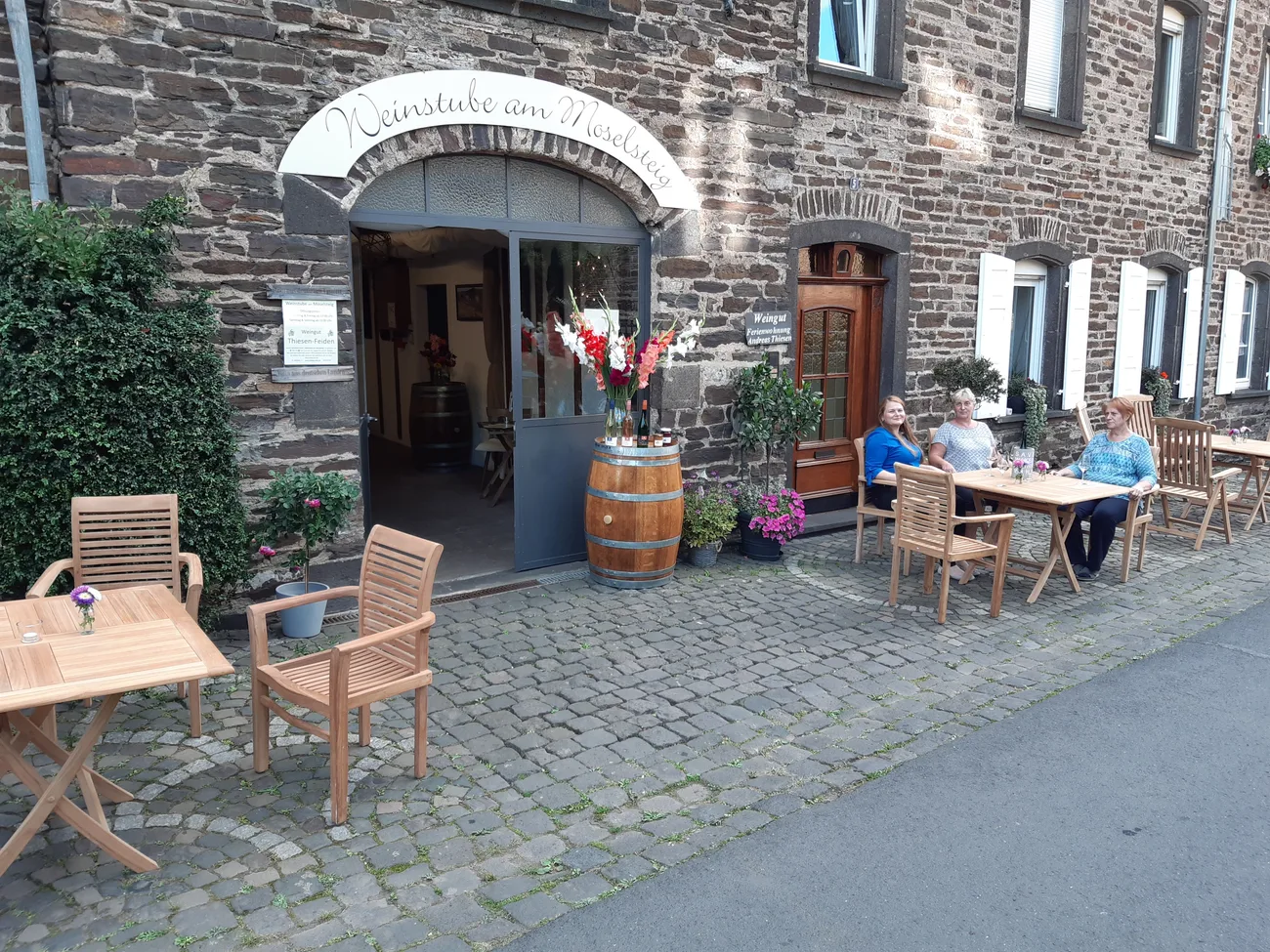 Eingang der Weinstube am Moselsteig mit Tischen und Weinfässern